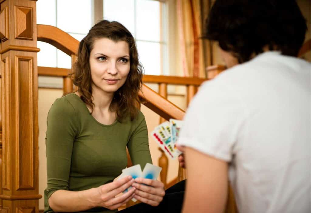 A woman with brown hair playing cards, focusing intently on the game as she sits on stairs opposite another player during their date night.