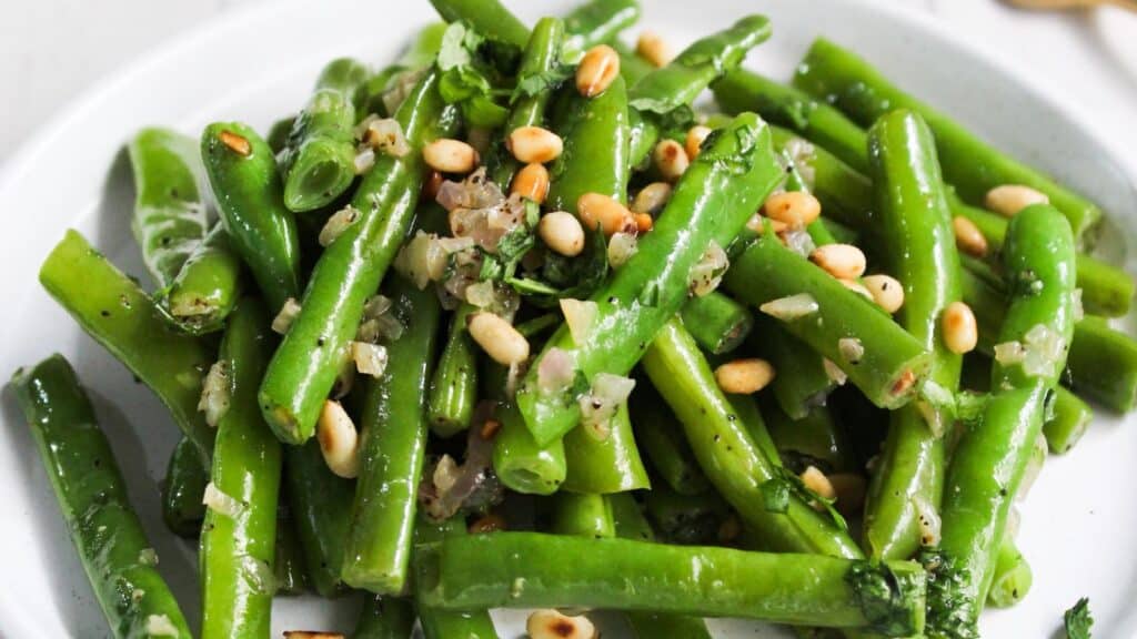 A dish of green beans topped with herbs and pine nuts.