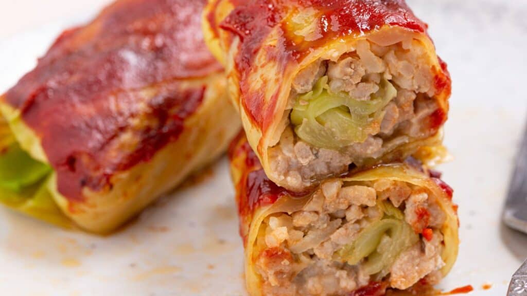 Stuffed cabbage rolls with meat and rice, cut open to reveal the filling, topped with tomato sauce.