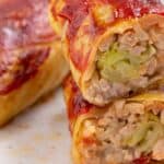 Stuffed cabbage rolls with meat and rice, cut open to reveal the filling, topped with tomato sauce.