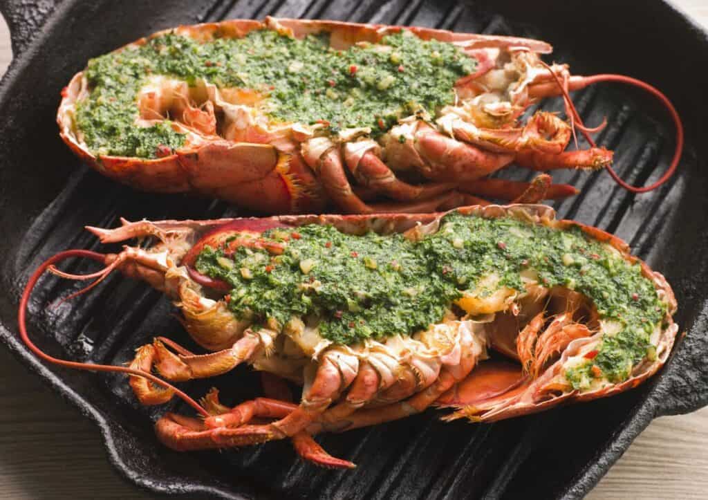 Grilled lobsters topped with herbs on a cast-iron pan.
