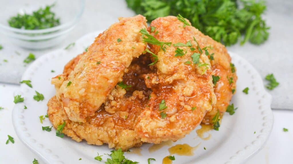 Golden-brown fried chicken with a honey glaze, garnished with fresh parsley on a white plate.
