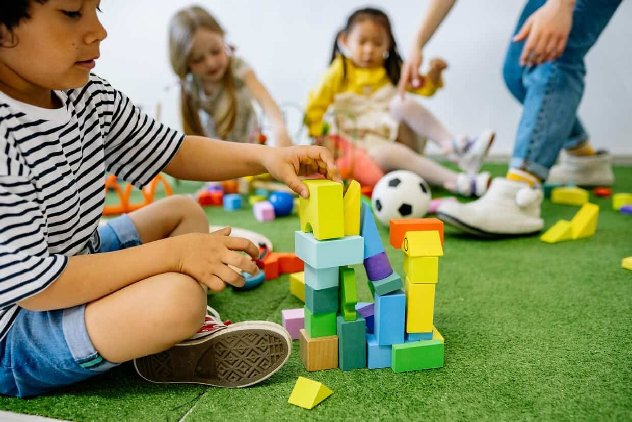 Children engage in activities for preschoolers with building blocks on the floor in a colorful playroom while adults supervise.