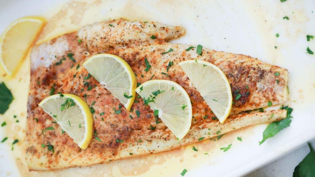Baked lemon butter fish fillet seasoned with herbs and spices, garnished with lemon slices and chopped parsley,.