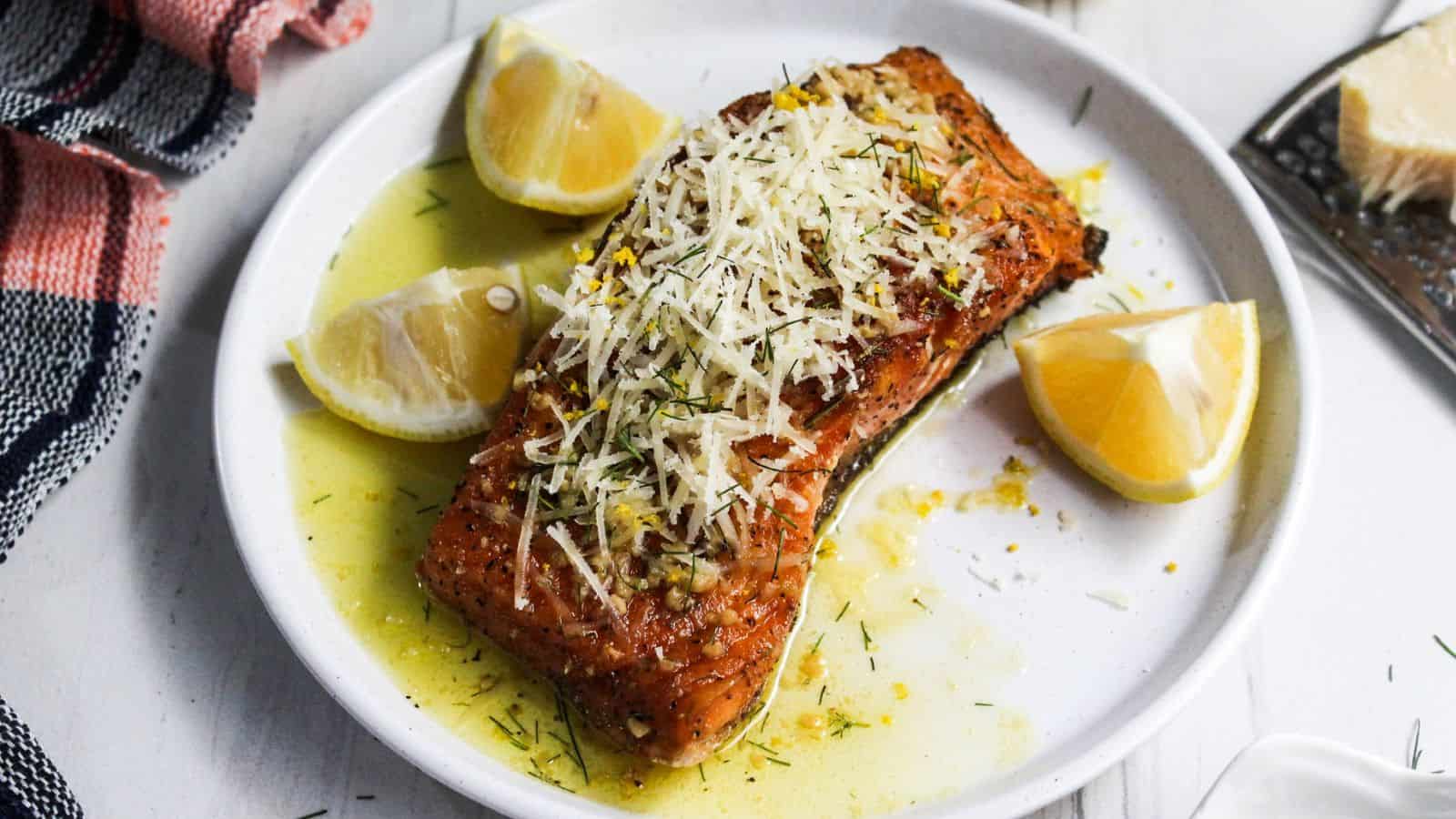 A plate of salmon on a white plate with lemon slices on it.