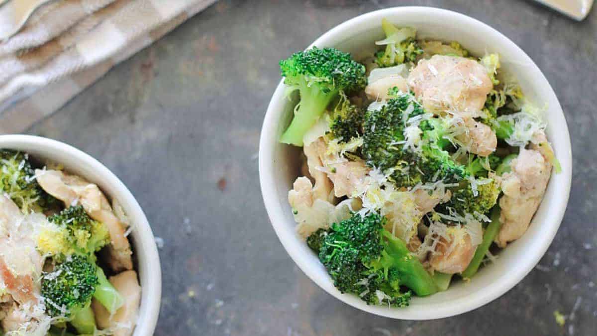 A bowl of chicken and broccoli with grated cheese on top.