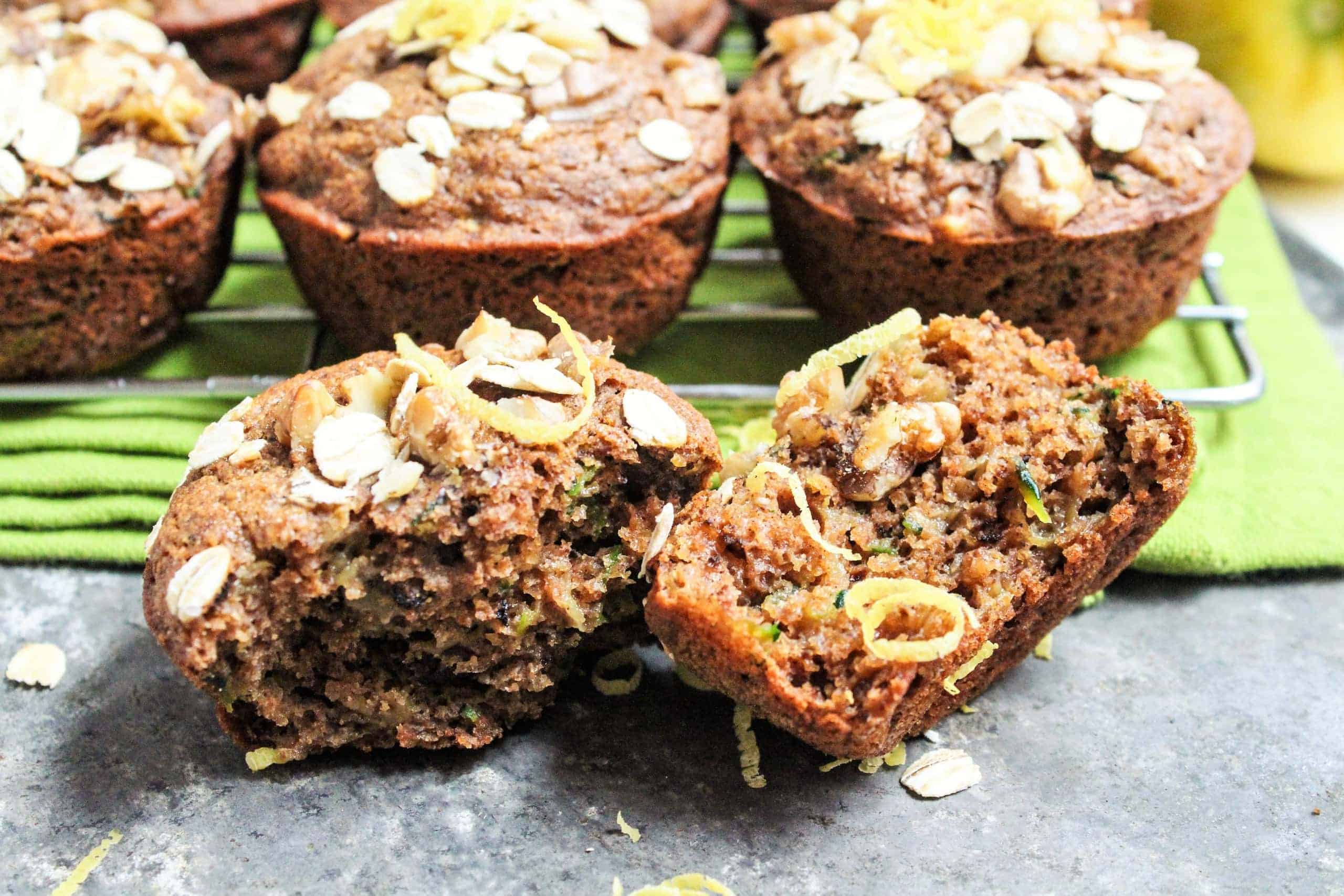 Lemon zucchini muffins torn in half sitting on a metal sheet pan with a green linen napkin behind it.