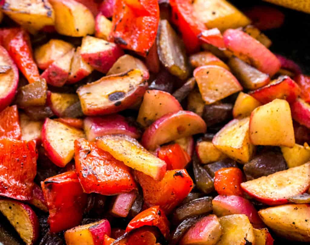 Close-up of a skillet with sautéed red peppers and chopped potatoes.