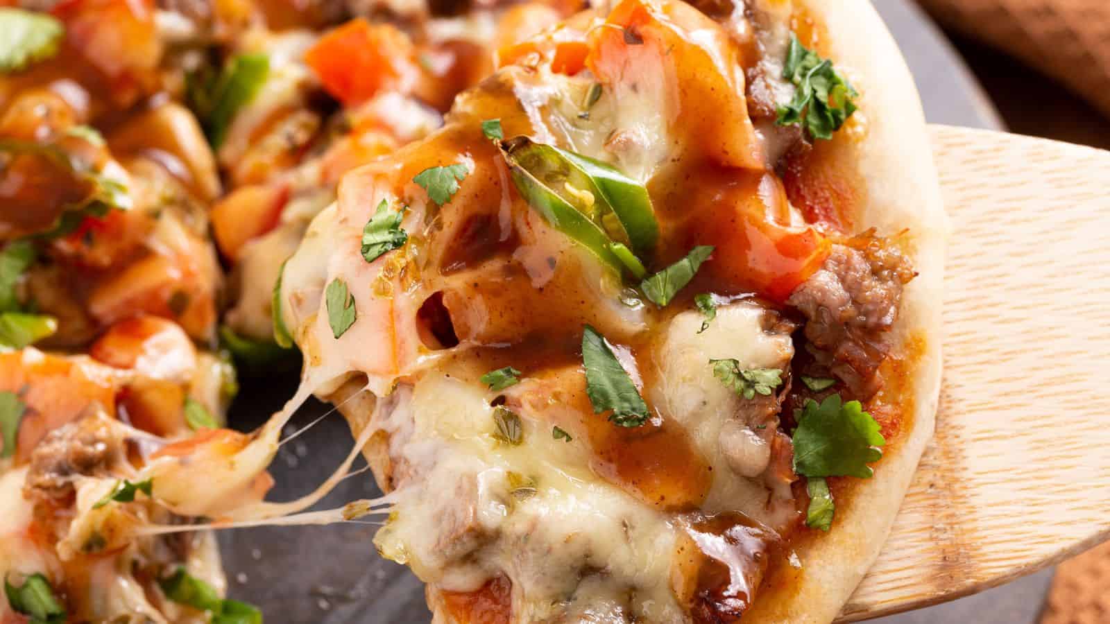 Close-up of a cheesy Mexican steak pizza on a wooden spatula.