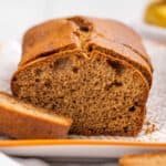 Sliced banana bread on a white plate with a geometric pattern, with a whole banana in the background.