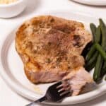 Oven baked pork steak on a plate with green beans and a fork on the side.