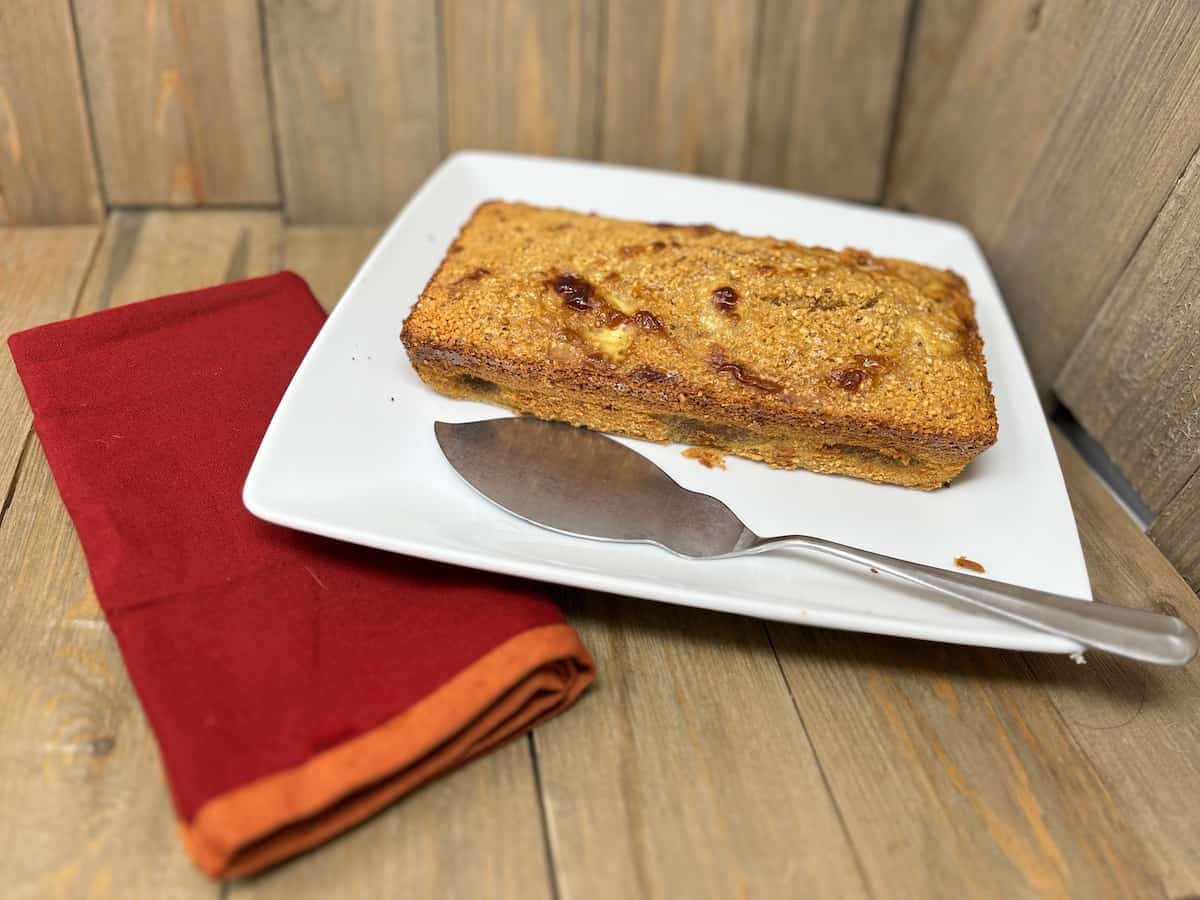 A slice of bread with jam served on a white plate beside a red napkin and a silver knife.