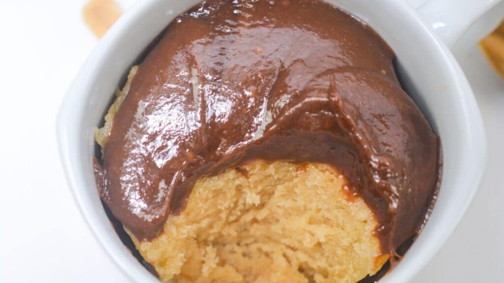 A peanut butter mug cake topped with glossy chocolate sauce, photographed from above on a white surface.