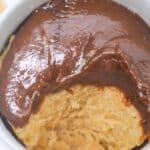 A peanut butter mug cake topped with glossy chocolate sauce, photographed from above on a white surface.