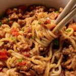 A bowl of noodles with meat sauce garnished with herbs, with a fork twirling some noodles.