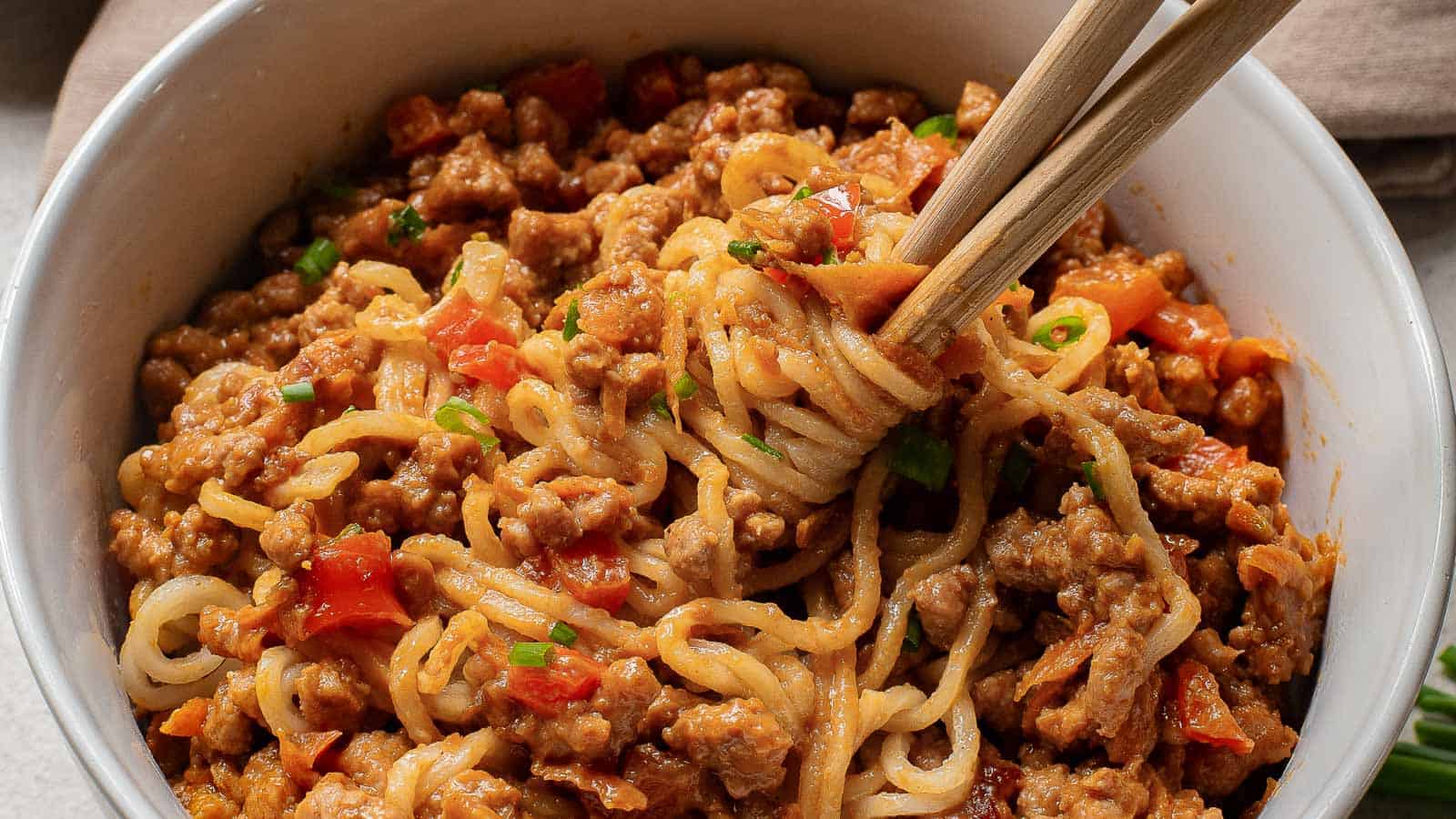A bowl of noodles with meat sauce garnished with herbs, with a fork twirling some noodles.