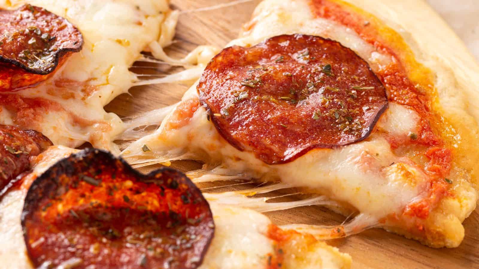 Close-up of a pepperoni pizza slice being lifted, showing melted cheese and tomato sauce.