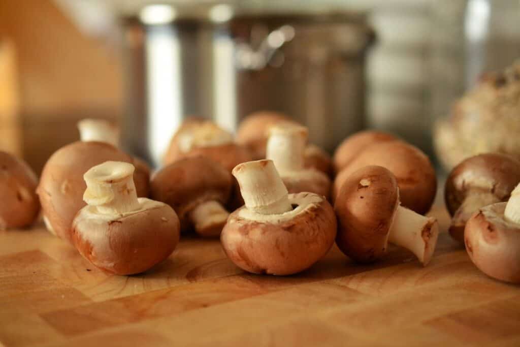A close-up of fresh, whole brown mushrooms on a wooden cutting board in a kitchen setting.
