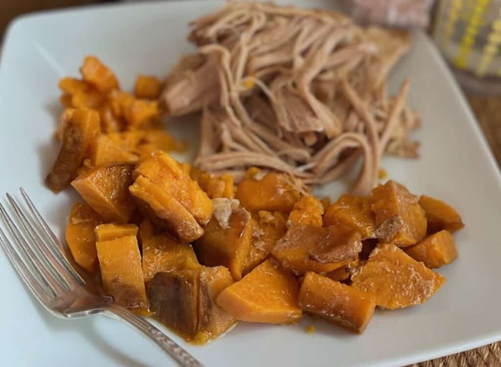 A plate of shredded turkey and cubed sweet potatoes, served with a fork on the side.