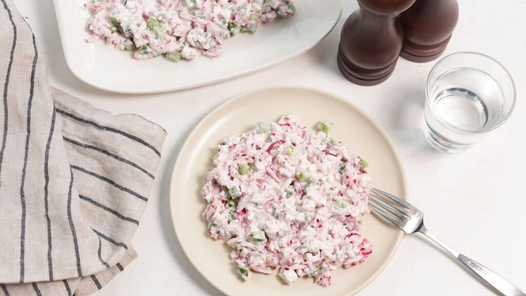 A plate of radish salad served on a table with a napkin, salt and pepper shakers, and a glass of water.