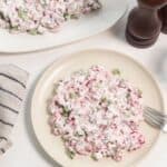 A plate of radish salad served on a table with a napkin, salt and pepper shakers, and a glass of water.