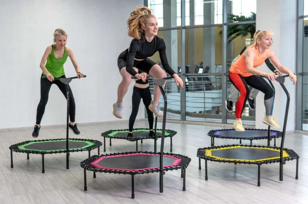 Three women exercising on mini trampolines in a spacious, brightly lit room.