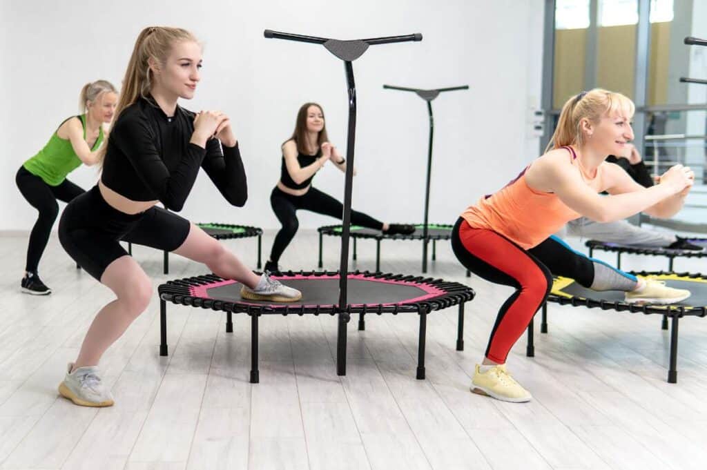 Four women of various ages exercising on mini trampolines in a bright, modern gym.