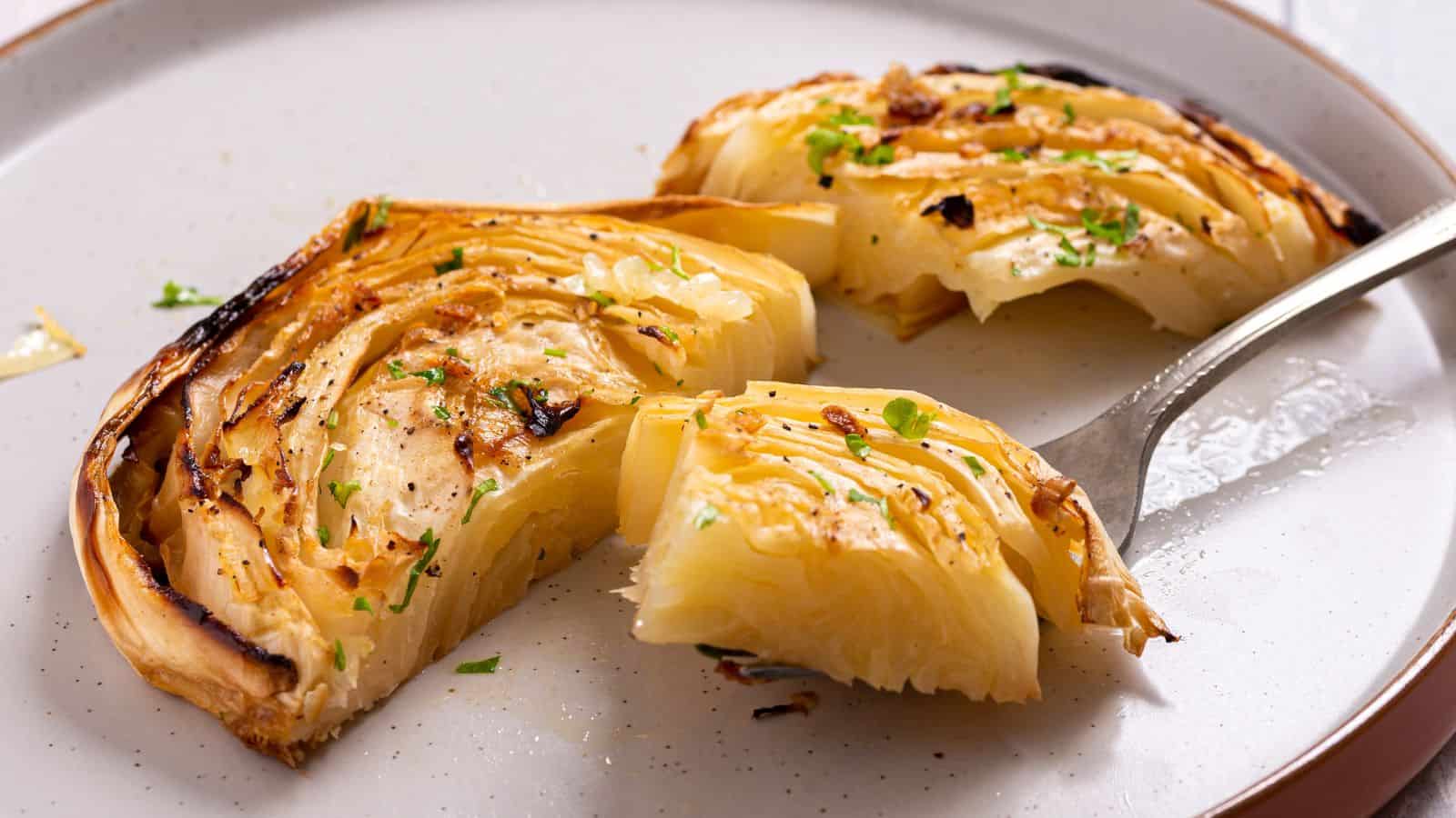 Sliced and roasted cabbage wedges seasoned with herbs on a white plate, garnished with black pepper and fresh herbs.
