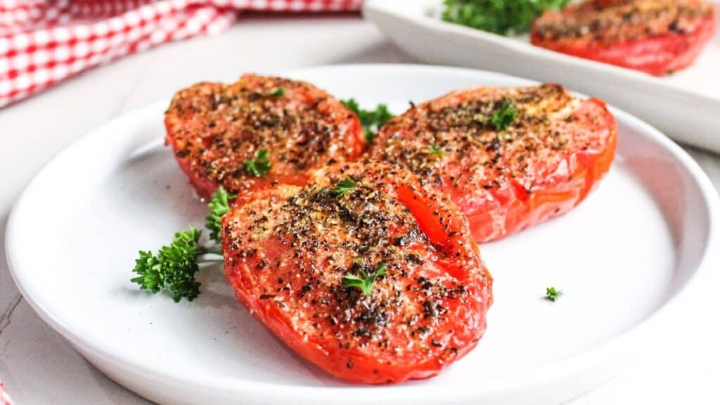 Roasted tomatoes seasoned with herbs and spices, served on a white plate garnished with parsley.