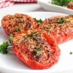 Roasted tomatoes seasoned with herbs and spices, served on a white plate garnished with parsley.