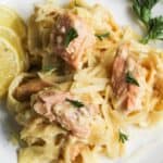 A plate of creamy pasta with salmon chunks, garnished with lemon slices and parsley.
