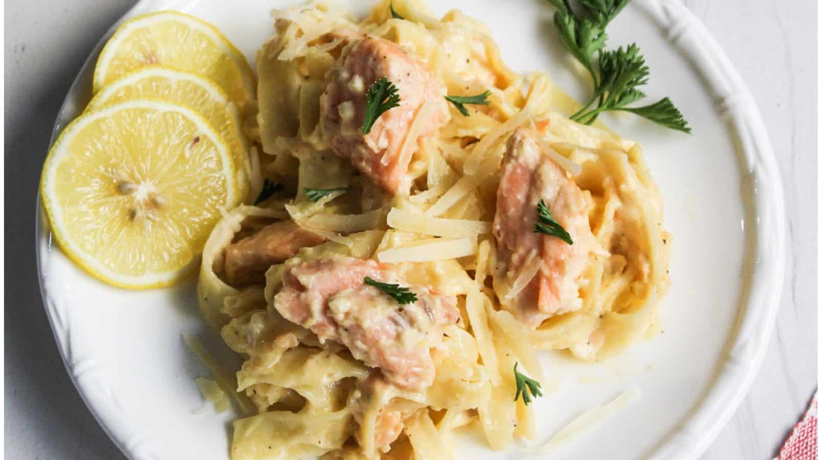 Salmon pasta Alfredo served on a white plate with lemon.