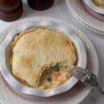 A seafood pot pie with a golden crust served in a white bowl, with a fork taking a bite out, revealing the creamy filling with vegetables.