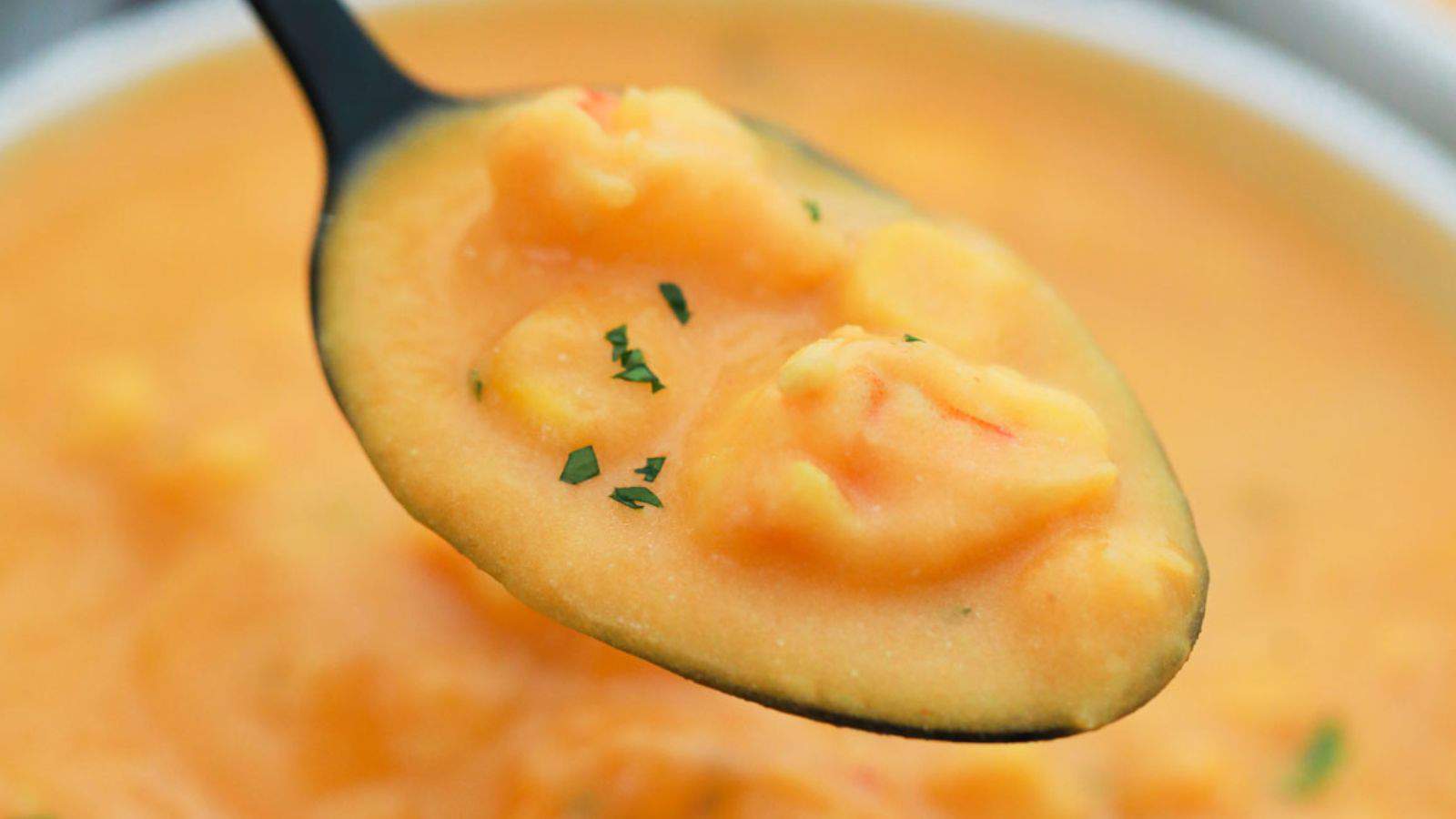 A close-up image of a spoonful of creamy shrimp bisque garnished with herbs, hovering above the rest of the soup in a bowl.