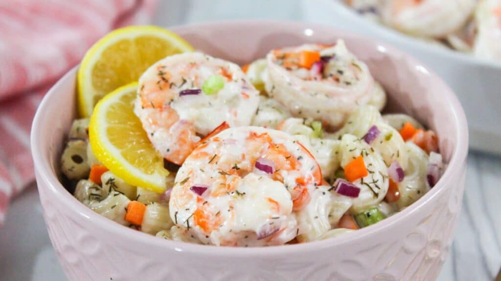 A bowl of shrimp pasta salad garnished with lemon slices and chopped vegetables.
