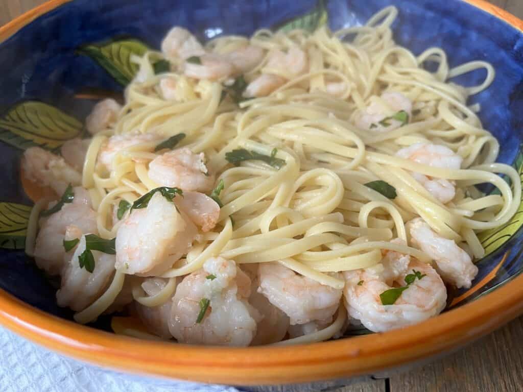 A blue bowl containing spaghetti and shrimp garnished with herbs, placed on a wooden table.