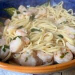 A blue bowl containing spaghetti and shrimp garnished with herbs, placed on a wooden table.