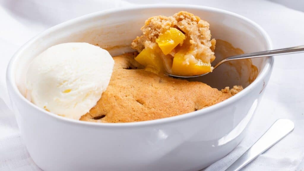 Peach cobbler served with a scoop of vanilla ice cream in a white bowl.