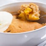 Peach cobbler served with a scoop of vanilla ice cream in a white bowl.