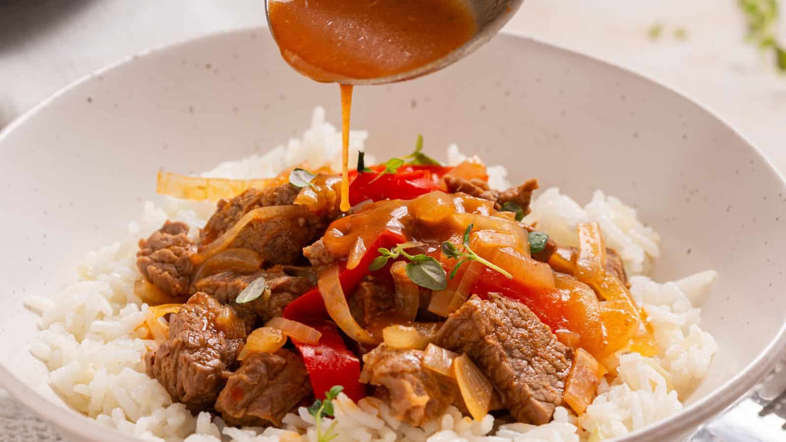 Pouring savory sauce over a bowl of rice topped with beef and bell peppers.