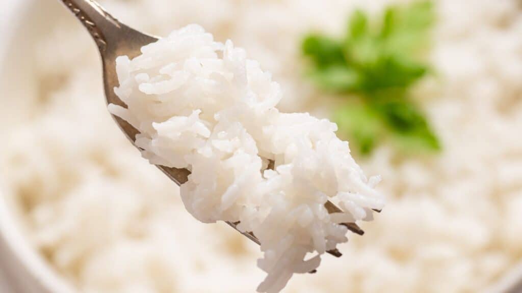 A spoonful of slow-cooked white rice held above a bowl, with a fresh green parsley leaf in the background.