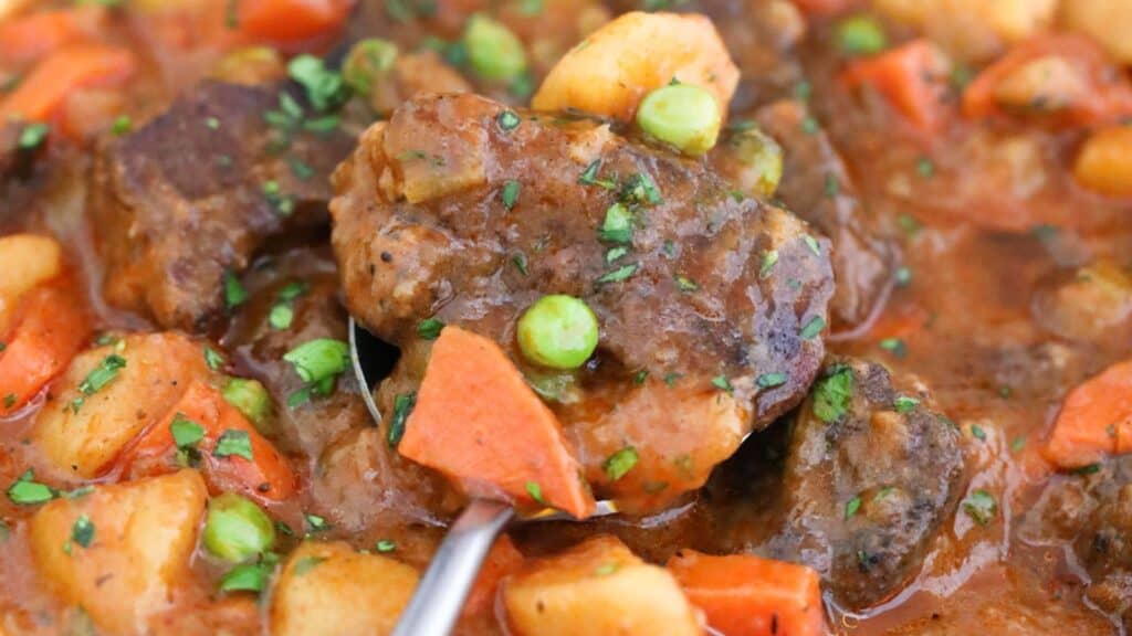 Beef stew with carrots, peas, and potatoes garnished with herbs.