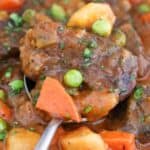 Beef stew with carrots, peas, and potatoes garnished with herbs.