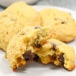 A plate with freshly baked chocolate chip cookies, one cookie is broken in half to show the soft inside.