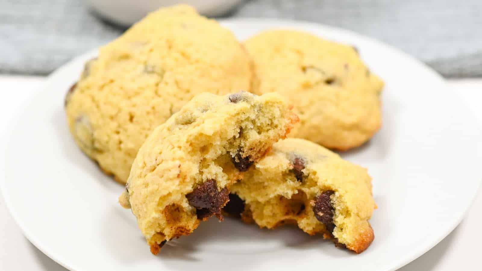 A plate with freshly baked chocolate chip cookies, one cookie is broken in half to show the soft inside.
