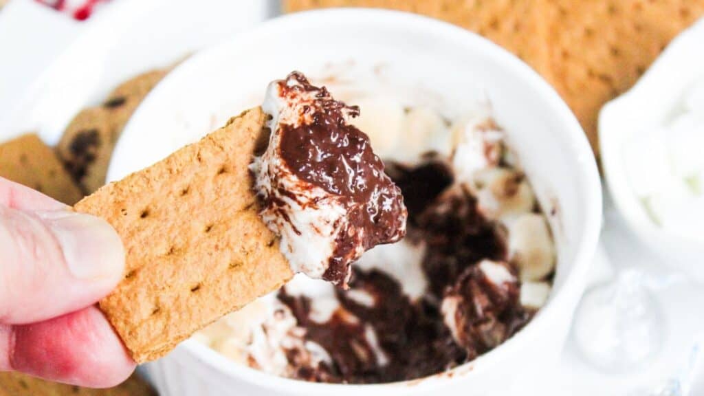 A person dipping a graham cracker into a bowl of chocolate dessert.