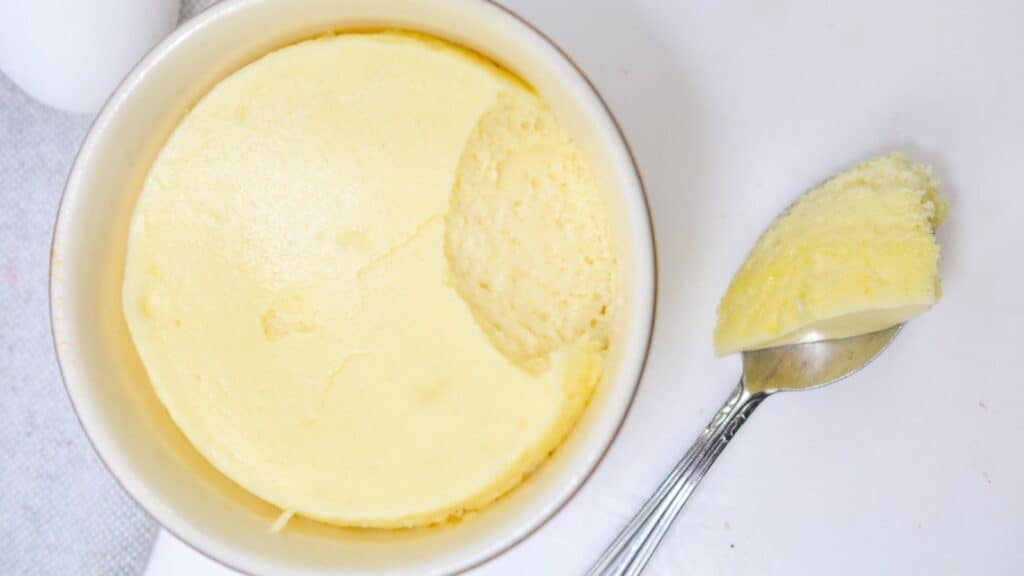 A serving of fresh, creamy cheesecake with a spoon taking a scoop out, placed on a white surface.