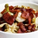 A bowl of sautéed cabbage topped with crispy bacon pieces.