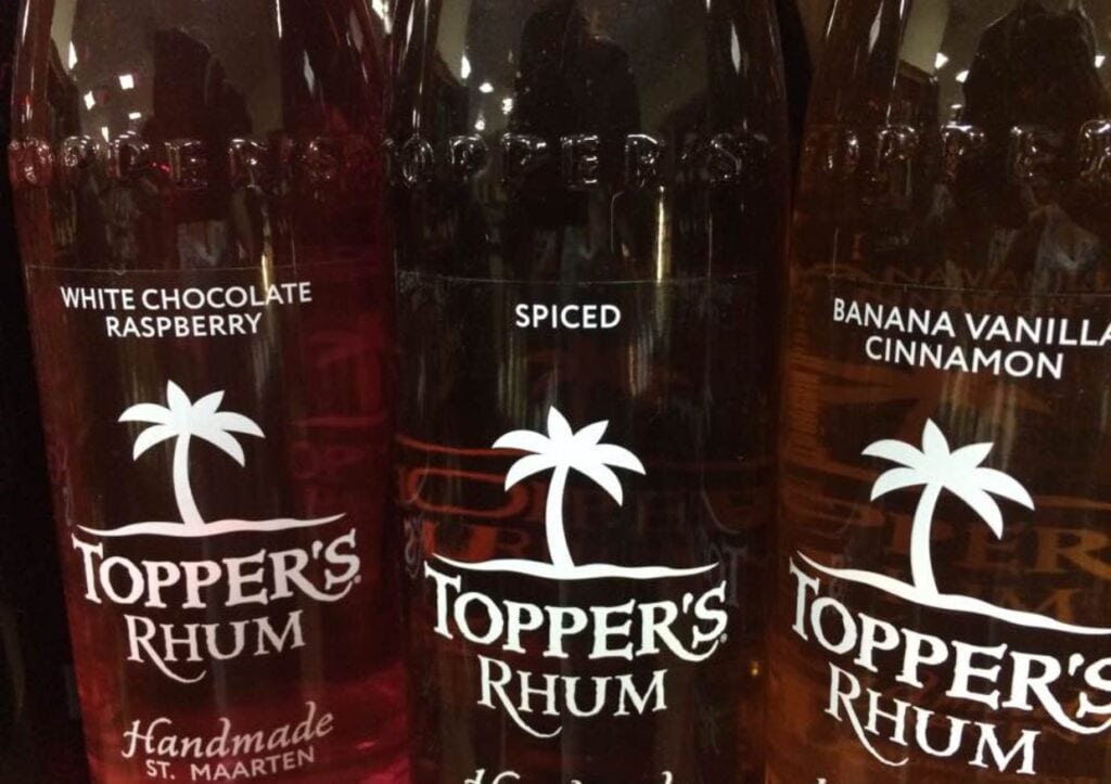 Assorted flavored topper's rhum bottles with labels indicating white chocolate raspberry, spiced, and banana vanilla cinnamon varieties.