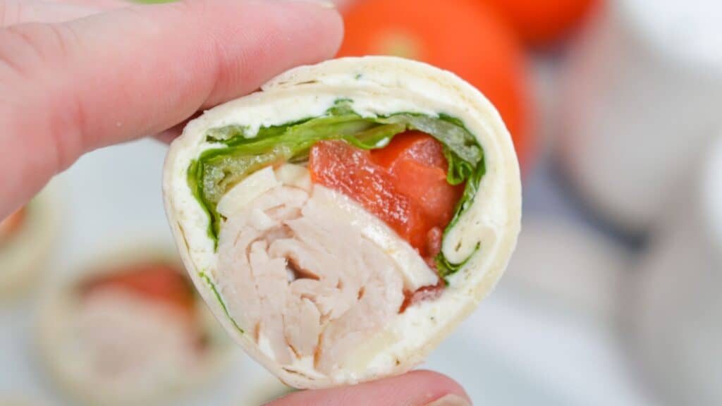 A close-up of a hand holding a turkey roll-up slice.